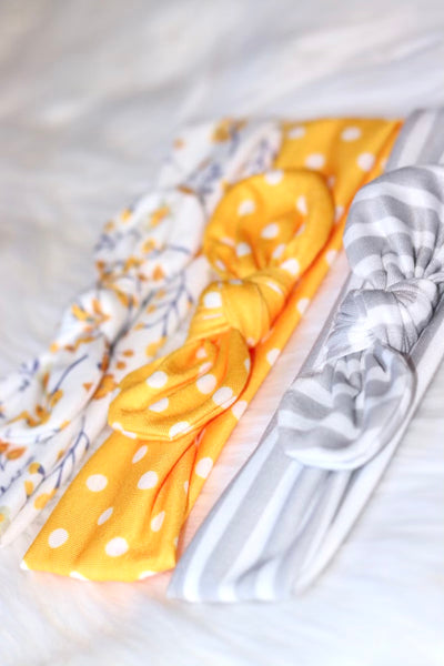 Stretchy grow-with-me set of three coordinating infant headbands with center bow, bright yellow polka dot, gray and white stripe, white and yellow floral.