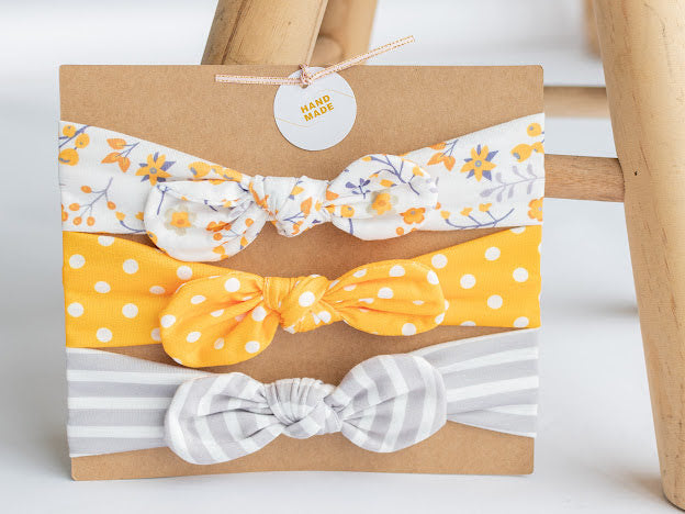 Stretchy grow-with-me set of three coordinating infant headbands with center bow, bright yellow polka dot, gray and white stripe, white and yellow floral.